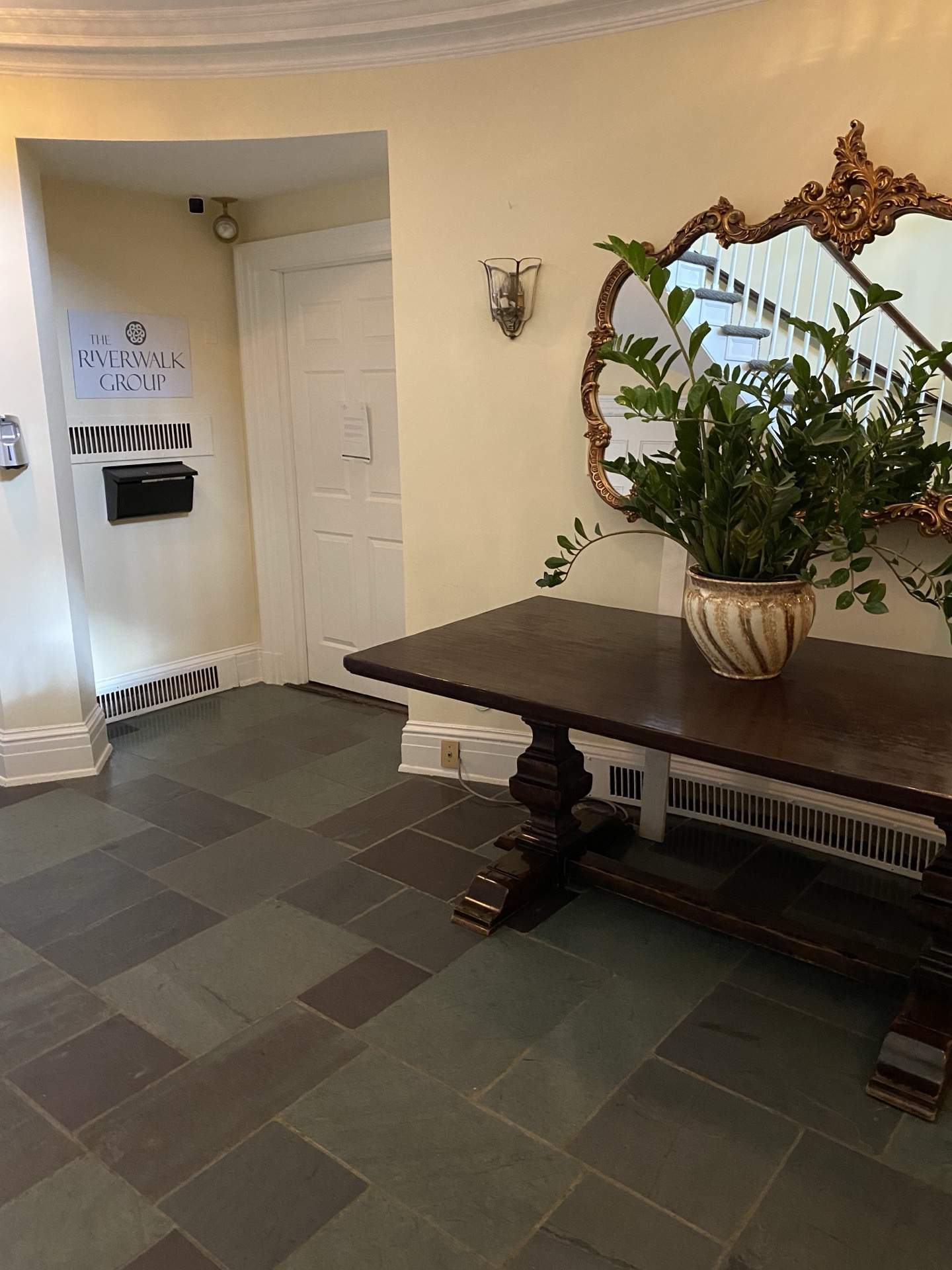 Ornate gilded mirror, potted fern, and slate tile flooring in the foyer of The Phillips Mansion